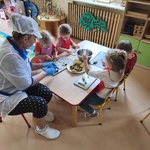 Dzieci siedzą przy stolikach i kroją owoce