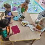 Dzieci siedzą przy stolikach i kroją owoce