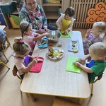Dzieci siedzą przy stolikach i kroją owoce