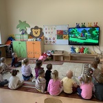 Grupa dzieci siedzi na dywanie z bohaterami programu